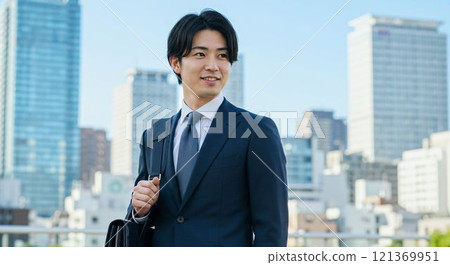 Young Japanese businessman in a suit carrying a business bag in a modern cityscape 121369951