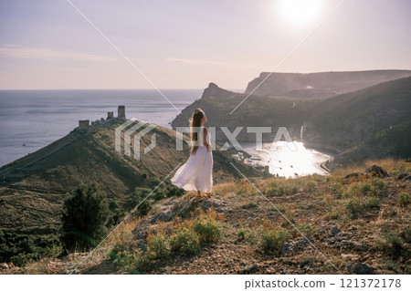woman stands on a hill overlooking the ocean, her arms raised in the air. Concept of freedom and joy, as if the woman is celebrating a moment of happiness or accomplishment. 121372178