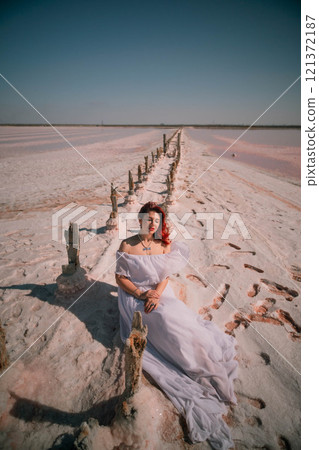 Woman Pink Salt Lake Photo Shoot - A woman in a white dress poses on a wooden boardwalk in a pink salt lake. 121372187