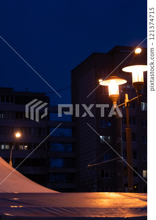 Soviet panel houses in the distance in the evening. A burning street lamp 121374715