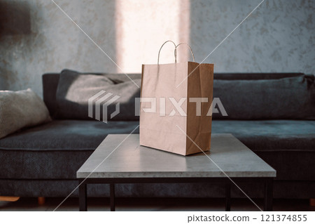Disposable bag of kraft paper with products left by courier of food delivery service on a table at home. Copy space. Kraft design. 121374855