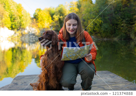 Happy 30s woman hiker hiking in mountain lake. Female with a irish setter dog looking at map and planning trip or get lost. Happy 30s woman hiker hiking in mountain lake. Female with a irish setter dog looking at map and planning trip or get lost. 121374888