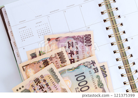 Japanese yen bills are arranged on an open calendar symbolizing budget planning savings, notebook gold spiral neat calendar layout organized feel Japanese yen bills are arranged on an open calendar symbolizing budget planning savings, notebook gold spiral neat calendar layout organized feel 121375399