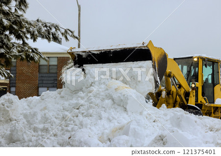 Snow loader is actively clearing heavy snow piles from residential streets during winter storm. Snow loader is actively clearing heavy snow piles from residential streets during winter storm. 121375401