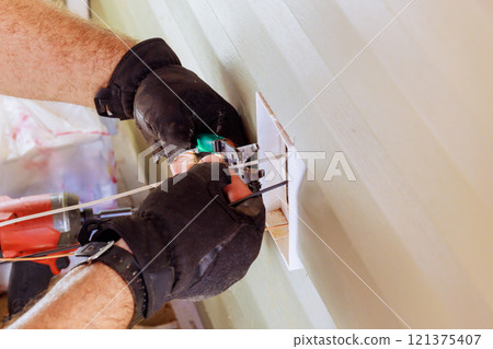 During electrical installation on exterior facade of house, electrician connects installs electrical outlets sockets 121375407
