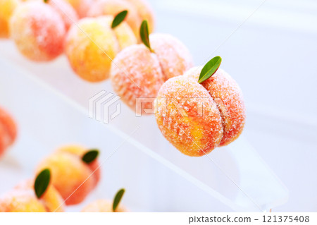 Charming peach shaped sweets are artfully arranged, showcasing blend of orange pink hues with delicate green leaves. 121375408