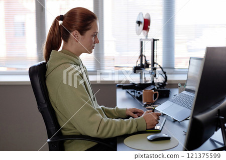 Caucasian woman sitting at desk using computer with focused expression in modern office setting surrounded by technology and equipment Caucasian woman sitting at desk using computer with focused expression in modern office setting surrounded by technology and equipment 121375599