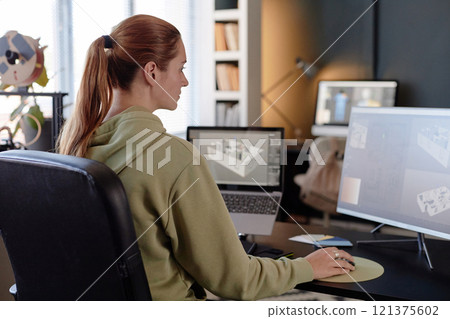 Professional designer engrossed in creating a 3D model on a computer screen with a modern workspace in the background including various gadgets and office decor 121375602