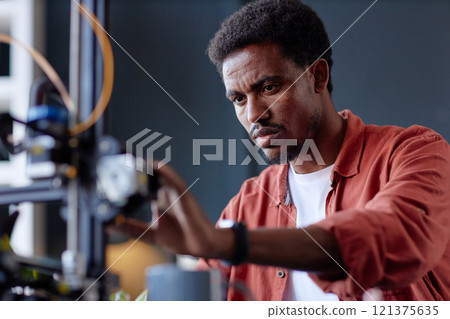 Black person concentrating on operating 3D printer in a workshop, adjusting settings for precise output. Technical task performed with focus on device intricacies in controlled environment 121375635
