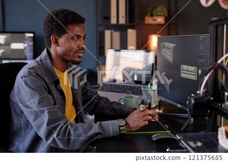 Man working at desk using computer to design 3D models of furniture Lighting from screens and multiple monitors enhancing workspace ambiance 121375685