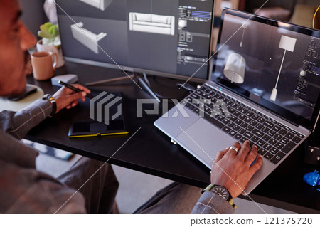 Designer is focusing on creating detailed interior models on laptop while using graphic tablet and multitasking in modern creative studio Designer is focusing on creating detailed interior models on laptop while using graphic tablet and multitasking in modern creative studio 121375720