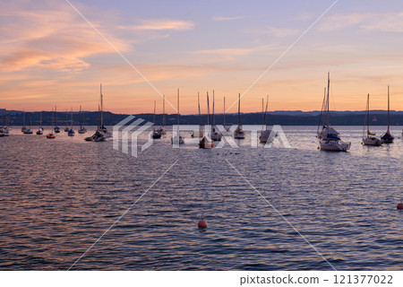 Sunset over Lake with Pier and Sailboats, Serene Waterfront Scene, Orange and Pink Sky, Calm Water, Silhouettes of Boats, Tranquil Evening, Reflections on Water, Peaceful Marina, Dusk Landscape 121377022