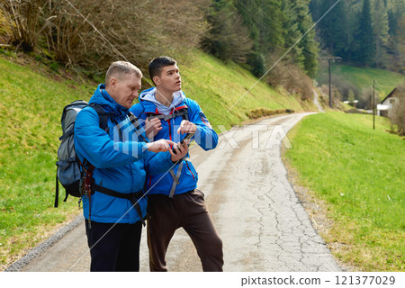 Two hikers are in the mountains in the spring nature outdoor. Hiking with backpacks. Two friends travel together in picturesque places. The man shows the way. Two men on a hiking trip in the mountains 121377029
