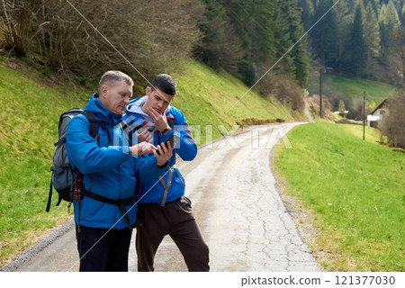 Two hikers are in the mountains in the spring nature outdoor. Hiking with backpacks. Two friends travel together in picturesque places. The man shows the way. Two men on a hiking trip in the mountains 121377030
