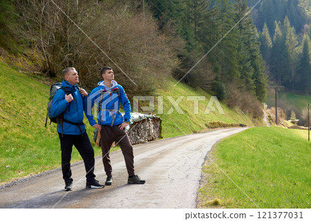Two hikers are in the mountains in the spring nature outdoor. Hiking with backpacks. Two friends travel together in picturesque places. The man shows the way. Two men on a hiking trip in the mountains 121377031