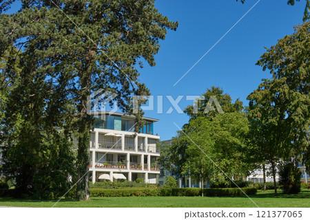 Luxurious High-Rise Building Nestled in Lush Green Park with Clear Blue Sky. Architectural Masterpiece Harmoniously Blends with Nature Showcasing Urban Ecology and Sustainable Living. 121377065