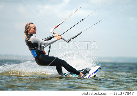 Close-up of kiteboarder preparing to jump during kitesurfing. Concentrated sportswoman riding fast on waves under sail Close-up of kiteboarder preparing to jump during kitesurfing. Concentrated sportswoman riding fast on waves under sail 121377847