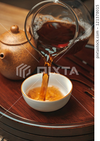 Pouring a steaming cup of tea from a clear teapot into a beautifully styled small cup Pouring a steaming cup of tea from a clear teapot into a beautifully styled small cup 121378015