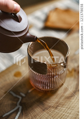 Pouring tea meticulously from a charming teapot into a delicate glass cup brings joy 121378038