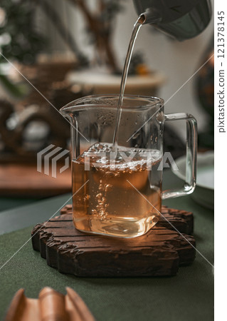 Pouring aromatic tea into a beautiful glass jug, surrounded by various natural elements Pouring aromatic tea into a beautiful glass jug, surrounded by various natural elements 121378145