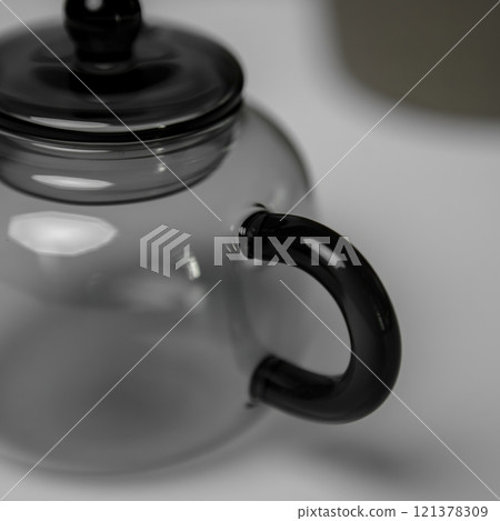 An elegant clear glass teapot with a stylish black handle for tea ceremonies and gatherings 121378309