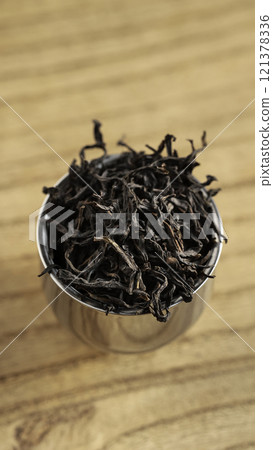 A Collection of Dried Tea Leaves Resting in a Metal Scoop on a Smooth Wooden Surface A Collection of Dried Tea Leaves Resting in a Metal Scoop on a Smooth Wooden Surface 121378336