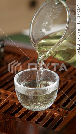 Pouring a soothing and fragrant tea into a delicate glass cup, enhancing the experience Pouring a soothing and fragrant tea into a delicate glass cup, enhancing the experience 121378384