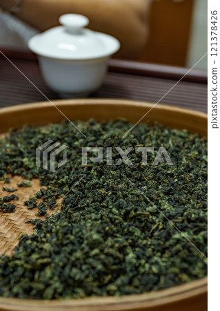 Closeup of loose green tea leaves next to a teapot, symbolizing a calming beverage ritual 121378426