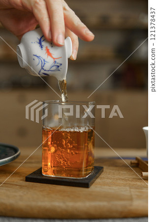 Pouring Tea from a Beautifully Crafted Traditional Teapot into a Delicate Glass Container 121378437