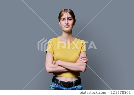 Beautiful smiling young girl with crossed arms looking at camera on grey background 121378501