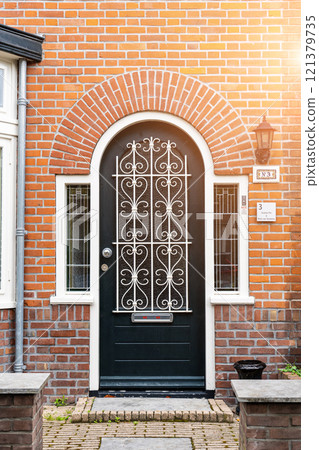 Wooden front door of a home. Front view of a wooden front door on a brick house with windows plants and a wide view of the porch and front walkway. Horizontal shot. 121379735