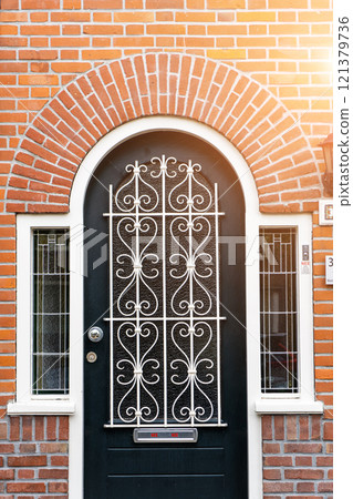 Wooden front door of a home. Front view of a wooden front door on a brick house with windows plants and a wide view of the porch and front walkway. Horizontal shot. 121379736