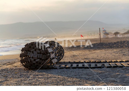 Outdoor roll out wooden beach pathway on the seashore, red flags in background, vacation and relaxation concept, sunrise, summer sunny day 121380058