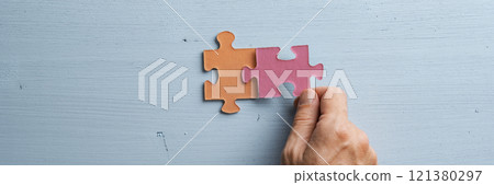 Wide view image of male hand joining two matching colorful puzzle pieces Wide view image of male hand joining two matching colorful puzzle pieces 121380297