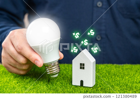 Save electricity at home and gain money. Utilities services. Save on bills. A man holds a glowing light bulb near a house. 121380489