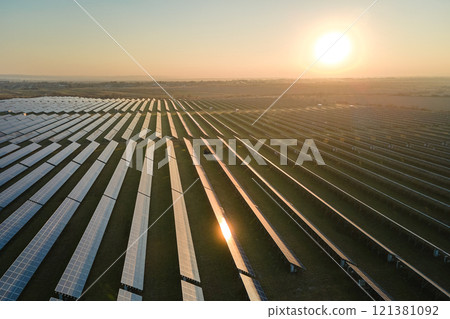 Aerial view of big sustainable electric power plant with many rows of solar photovoltaic panels for producing clean electrical energy at sunset. Renewable electricity with zero emission concept Aerial view of big sustainable electric power plant with many rows of solar photovoltaic panels for producing clean electrical energy at sunset. Renewable electricity with zero emission concept 121381092