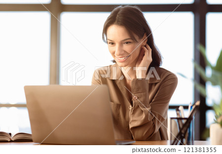 Happy Student. Portrait of smiling girl using laptop, sitting at office and touching her neck, copyspace 121381355