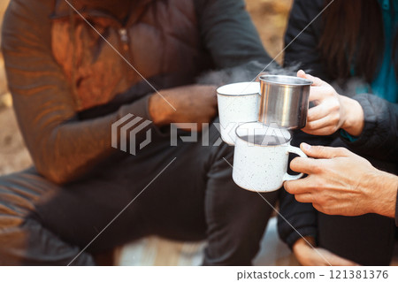 Warming up in camping. Hands of international hikers cheering up with camping cups, camping in forest, closeup 121381376