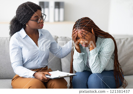 Upset black lady with nervous breakdown consulting psychologist, having session with counselor at clinic. Professional psychotherapist comforting depressed female patient at office 121381437