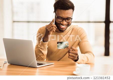 Online Shopping. Millennial black guy holding credit card and talking on smartphone. Free space 121381452