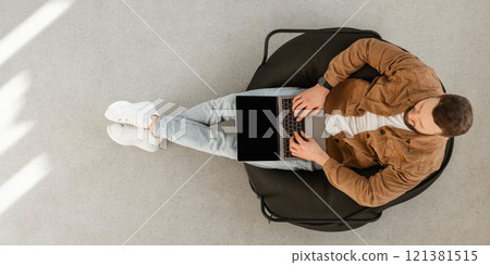 Male Freelancer Using Laptop Computer With Blank Screen Sitting In Chair At Home. Technology And Gadgets, Freelance Career And Lifestyle Concept. Top View Shot, Panorama, Mockup Male Freelancer Using Laptop Computer With Blank Screen Sitting In Chair At Home. Technology And Gadgets, Freelance Career And Lifestyle Concept. Top View Shot, Panorama, Mockup 121381515
