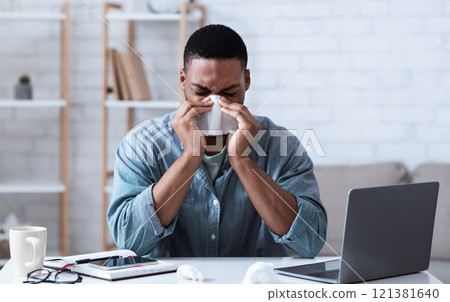 Sick Black Guy Working In Office, Sitting At Laptop And Blowing Nose In Paper Napkin Indoors. Ill Employee Concept. African Man Having Cold, Rhinitis And Sinusitis Symptoms At Work. Sick Black Guy Working In Office, Sitting At Laptop And Blowing Nose In Paper Napkin Indoors. Ill Employee Concept. African Man Having Cold, Rhinitis And Sinusitis Symptoms At Work. 121381640