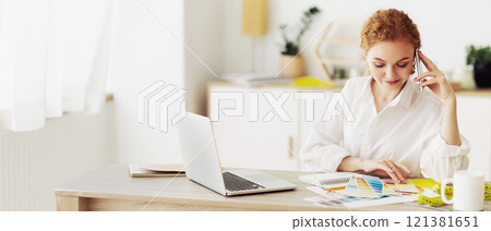 A woman is working on a design project, discussing ideas on the phone while looking at a color palette. 121381651