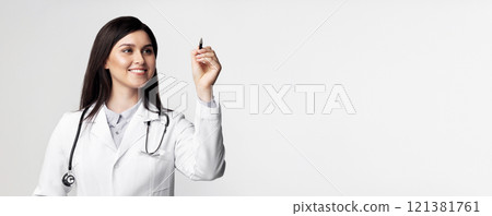 A female doctor in a white coat and stethoscope smiles while writing on a white board with a black marker. A female doctor in a white coat and stethoscope smiles while writing on a white board with a black marker. 121381761