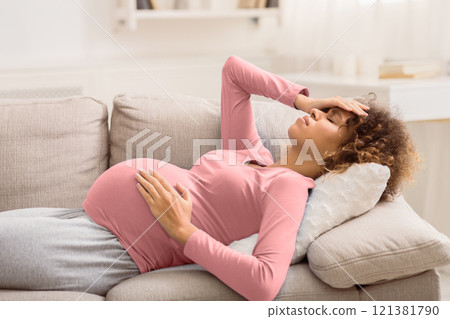 Young expectant woman with headache lying on sofa, touching her belly and forehead Young expectant woman with headache lying on sofa, touching her belly and forehead 121381790