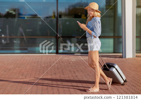 Tourist concept. Young girl traveler walking with suitcase against airport building Tourist concept. Young girl traveler walking with suitcase against airport building 121381814