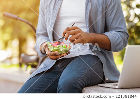 Unrecognizable African Man Eating Salad, Having Healthy Lunch Outdoors On Bench In Park, Cropped Image, Closeup, Selective Focus On Food 121381844