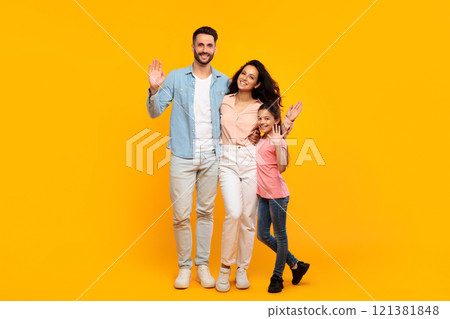 A happy family of three, a father, mother, and daughter, are standing in front of a bright yellow background. They are all smiling and waving, and they appear to be enjoying themselves. A happy family of three, a father, mother, and daughter, are standing in front of a bright yellow background. They are all smiling and waving, and they appear to be enjoying themselves. 121381848