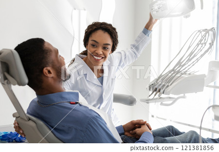 Beautiful black woman dentist greeting male patient on her workplace, copy space 121381856