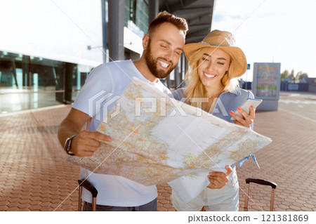 Newlyweds looking map and planning route in new city, standing against airport building 121381869